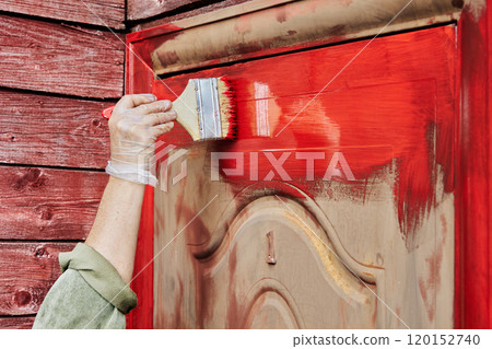 Painting metal entrance door of country house red using 100 mm wide flat brush. Painting metal entrance door of country house red using 100 mm wide flat brush. 120152740