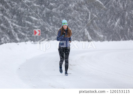 Woman Jogging Along a Snowy Road During a Blizzard in Winter Mountains Woman Jogging Along a Snowy Road During a Blizzard in Winter Mountains 120153115