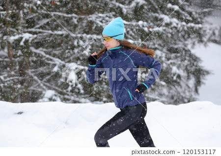 Woman Running in the Snowy Forest Wearing Winter Gear on a Snowy Day 120153117