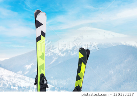 Two vibrant pairs of skis against distant mountains under a cloudy sky. Two vibrant pairs of skis against distant mountains under a cloudy sky. 120153137