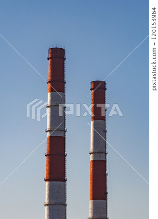 Two tall smokestacks stand against a clear blue sky, their red and white bands a stark contrast against the horizon 120153964