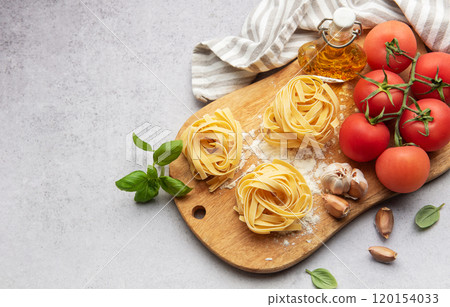 Tagliatelle pasta nests with tomatoes, garlic, basil and olive oil on wooden board Tagliatelle pasta nests with tomatoes, garlic, basil and olive oil on wooden board 120154033