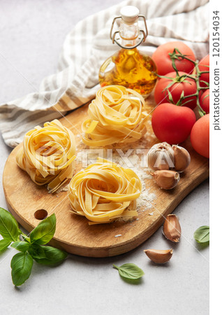 Tagliatelle pasta nests with tomatoes, garlic, basil and olive oil on wooden board Tagliatelle pasta nests with tomatoes, garlic, basil and olive oil on wooden board 120154034