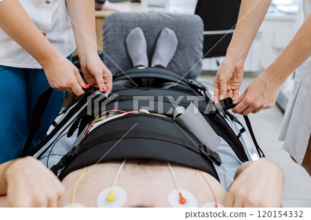 Medical professionals prepare patient with straps and electrodes for physical therapy session 120154332
