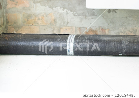 A roll of bituminous roofing material lies on a concrete floor. A roll of bituminous roofing material lies on a concrete floor. 120154483