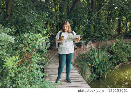 Stylish hipster woman holding paper map and phone, wearing backpack and relaxing in nature. Travel and wanderlust concept. Amazing chill moment, summer time. Full body Stylish hipster woman holding paper map and phone, wearing backpack and relaxing in nature. Travel and wanderlust concept. Amazing chill moment, summer time. Full body 120155061