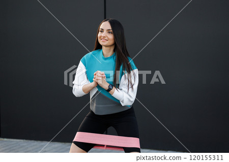 Woman training with elastic rubber resistance bands in outdoor in the city on dark wall background. 120155311