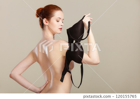 Naked woman holds black bra in hand 120155765