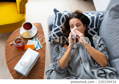 Woman is laying on a couch with a tissue Woman is laying on a couch with a tissue 120156418