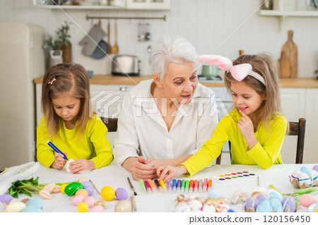 Happy Easter. Two little girls sisters twins grandmother painting eggs enjoying time together. Happy family grandma granddaughters child kids preparing for Easter. Spring Christian festival tradition Happy Easter. Two little girls sisters twins grandmother painting eggs enjoying time together. Happy family grandma granddaughters child kids preparing for Easter. Spring Christian festival tradition 120156450