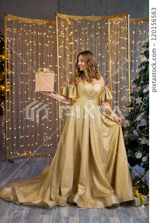 Fashion interior photo of beautiful sensual woman with Gift box in luxurious golden dress posing Fashion interior photo of beautiful sensual woman with Gift box in luxurious golden dress posing 120156563