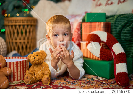Happy boy of 3 years old lies on floor of house next to Christmas tree with side of garlands and Happy boy of 3 years old lies on floor of house next to Christmas tree with side of garlands and 120156578