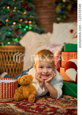 Happy boy of 3 years old lies on floor of house next to Christmas tree with side of garlands and Happy boy of 3 years old lies on floor of house next to Christmas tree with side of garlands and 120156586