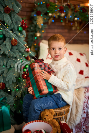 Cute boy hugging a gift box next to Christmas tree. A child in anticipation of miracles and a Cute boy hugging a gift box next to Christmas tree. A child in anticipation of miracles and a 120156607