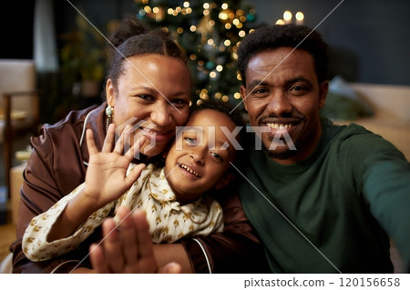 Front view portrait of happy Black family with little boy waving at camera smiling speaking to friends and family by video chat on Christmas 120156658