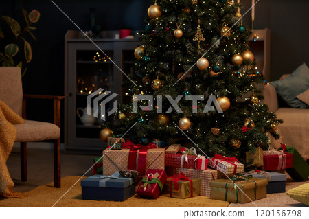 Background image of beautiful Christmas tree with gold accents and pile of presents in cozy home interior in low lighting copy space 120156798