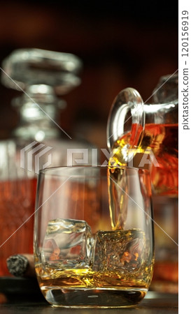Pouring whiskey into glass full of ice cubes. 120156919
