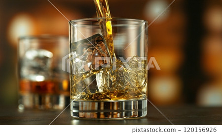 Pouring whiskey into glass full of ice cubes. Pouring whiskey into glass full of ice cubes. 120156926