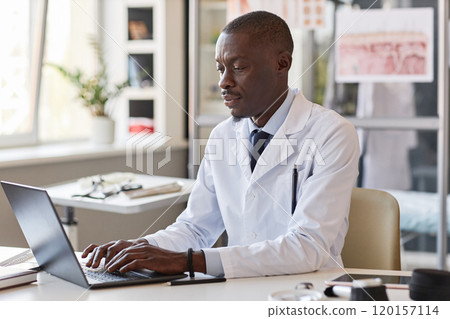 Portrait of adult African American man working as doctor in clinic and typing at laptop keyboard while sitting at desk copy space Portrait of adult African American man working as doctor in clinic and typing at laptop keyboard while sitting at desk copy space 120157114