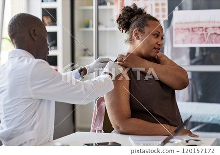Side view portrait of adult African American woman demonstrating mole or skin rash on back to doctor during examination in dermatology clinic 120157172