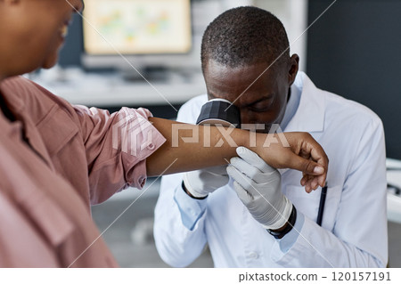Front view portrait of African American doctor looking in dermascope while examining patient at dermatology clinic copy space Front view portrait of African American doctor looking in dermascope while examining patient at dermatology clinic copy space 120157191