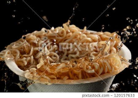 Instant noodle in soup bowl. Pouring soup on Noodle and spill splash. Noodle food is ramen Japanese soup Chinese. Black background isolated Instant noodle in soup bowl. Pouring soup on Noodle and spill splash. Noodle food is ramen Japanese soup Chinese. Black background isolated 120157633