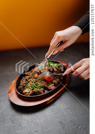 Tender grilled meat served on a sizzling plate with fresh herbs and tomatoes, ready to enjoy 120157637