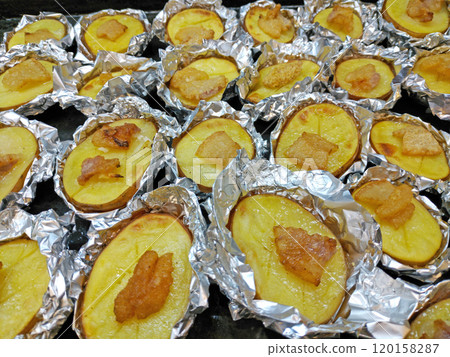 potato halves wrapped in foil and topped with pieces of lard or bacon 120158287