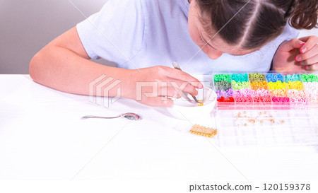 Delicate fingers of a young girl navigate through a treasure trove of bright, multicolored beads, each compartment revealing a new hue to choose from. 120159378
