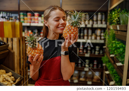 A Joyful Young Woman Cheerfully Holding Fresh Pineapples in a Grocery Store Today A Joyful Young Woman Cheerfully Holding Fresh Pineapples in a Grocery Store Today 120159493