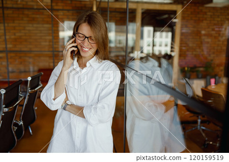 A Smiling Woman Engaged in a Phone Conversation in a Modern Office Environment full of Life A Smiling Woman Engaged in a Phone Conversation in a Modern Office Environment full of Life 120159519