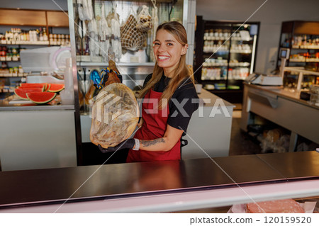A woman proudly holding a delectable ham in a gourmet grocery store, showcasing culinary delights A woman proudly holding a delectable ham in a gourmet grocery store, showcasing culinary delights 120159520