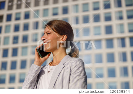 A professional woman talks on the phone, with modern architecture in the background 120159544