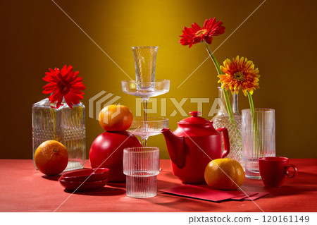 In the yellow backdrop, a close-up of a contemporary Tet banquet table with glass vases loaded with gerbera flowers, glasses, a tea set, tangerines, and fortunate envelopes laid on the red tabletop. 120161149
