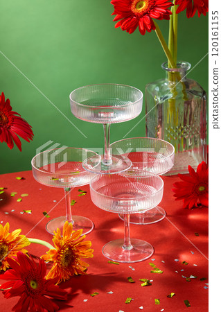 A close-up image of a modern Tet banquet table taken from above, features stacked cocktail glasses surrounded by gerbera daisies, glass vases, and confetti in the green background. A close-up image of a modern Tet banquet table taken from above, features stacked cocktail glasses surrounded by gerbera daisies, glass vases, and confetti in the green background. 120161155