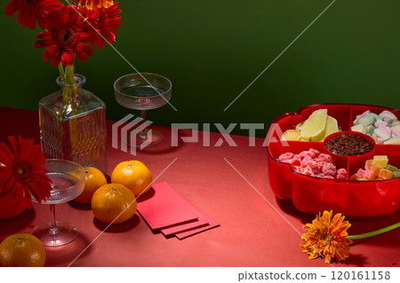 The green background in the side-angle photo of a contemporary Tet banquet table from above includes a red tray of jams, tangerines, glass vases, glasses, fortune envelopes, and Gerbera flowers. The green background in the side-angle photo of a contemporary Tet banquet table from above includes a red tray of jams, tangerines, glass vases, glasses, fortune envelopes, and Gerbera flowers. 120161158