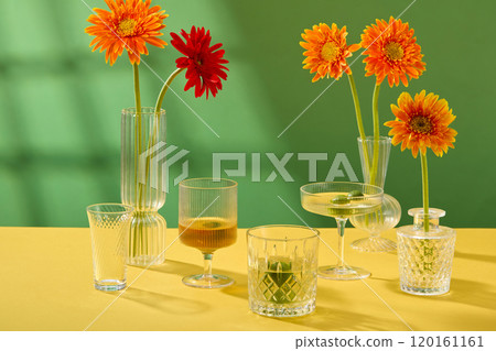 The still life picture template features a contemporary Tet theme with a green backdrop and a front view of water glasses next to flower vases filled with gerbera blossoms on a yellow table. 120161161