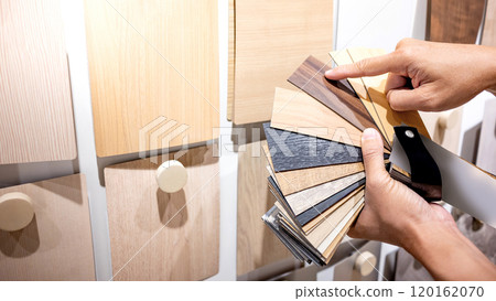 Designer hand pointing at sample of wood laminated from natural collection in material showroom 120162070