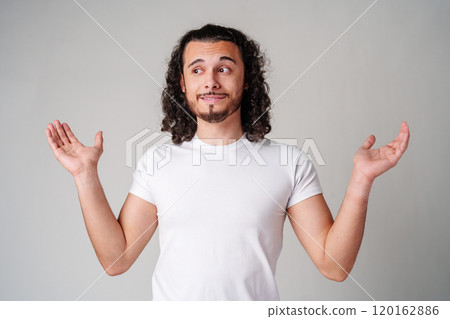 A man with curly hair expressing uncertainty while standing against a neutral background A man with curly hair expressing uncertainty while standing against a neutral background 120162886