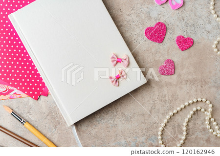 A collection of crafting materials arranged on a textured surface with a blank notebook, decorative paper, and various embellishments A collection of crafting materials arranged on a textured surface with a blank notebook, decorative paper, and various embellishments 120162946