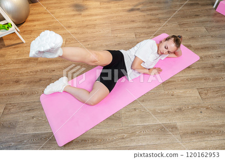 Woman doing floor exercises on a pink mat in a bright room 120162953