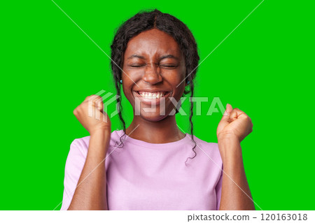 Joyful woman celebrating success with clenched fists against a bright green background 120163018