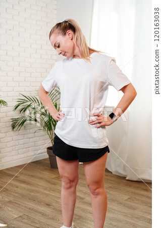 A woman stretches her neck and shoulders in a bright room surrounded by indoor plants 120163038