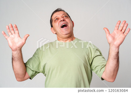 A middle-aged man with a neutral expression raises his hands in a questioning gesture against a plain backdrop A middle-aged man with a neutral expression raises his hands in a questioning gesture against a plain backdrop 120163084