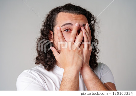 Young man covers his face with hands in a moment of surprise or shock against a neutral background 120163334