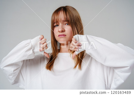Young teen girl expressing disapproval while wearing a white oversized sweater against a plain backdrop 120163489