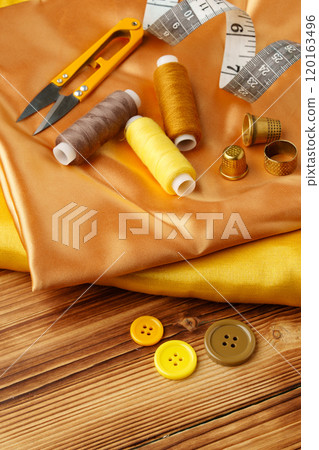 Crafting essentials arranged on golden satin fabric with sewing tools and colorful buttons scattered around 120163496