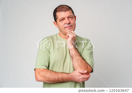 A man in a light green shirt and jeans stands against a plain background with a thoughtful expression 120163647