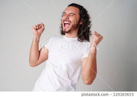 Happy man celebrating success with raised fists in a studio against a plain background 120163653