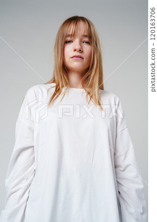 Young woman with long hair in a white sweatshirt standing against a light gray background Young woman with long hair in a white sweatshirt standing against a light gray background 120163706